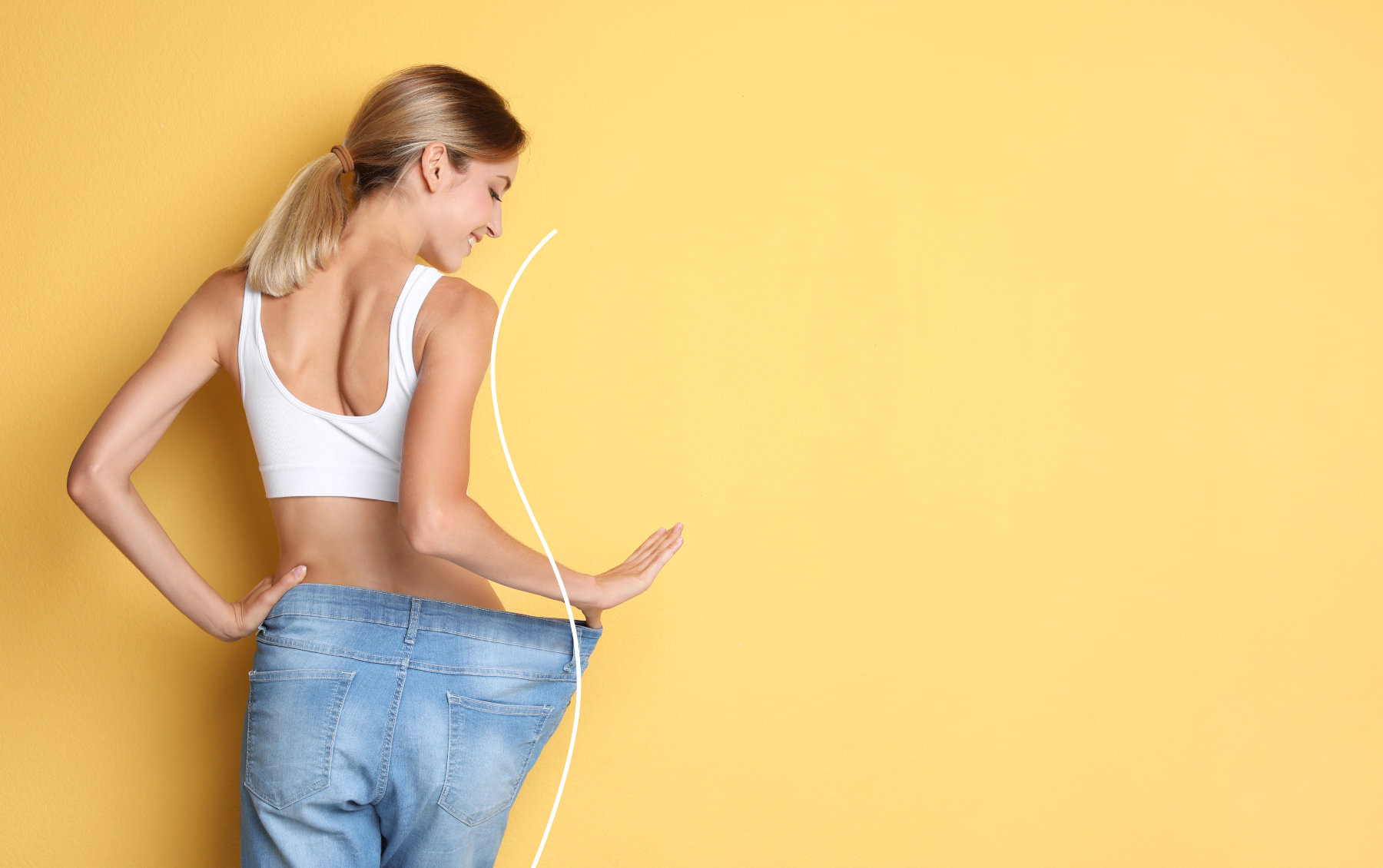 Happy young woman with slim body in oversized jeans on yellow ba