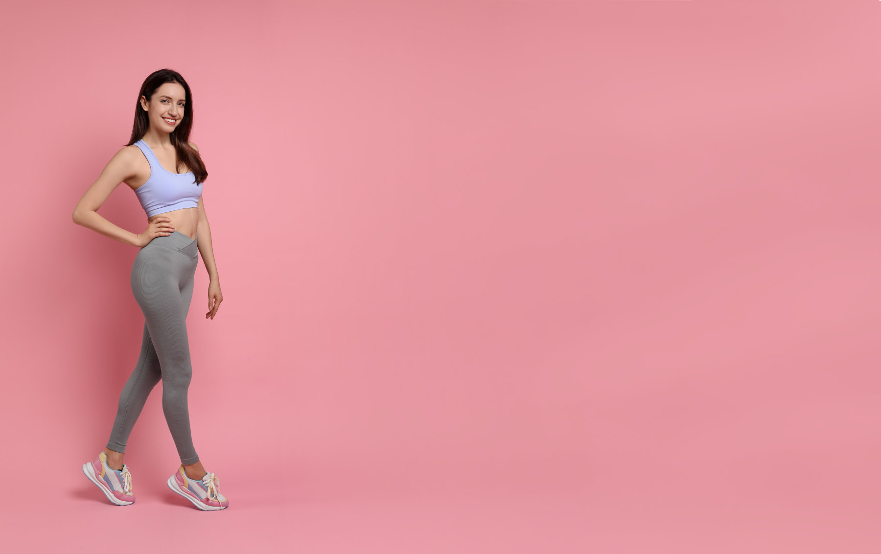 Happy young woman with slim body posing on pink background